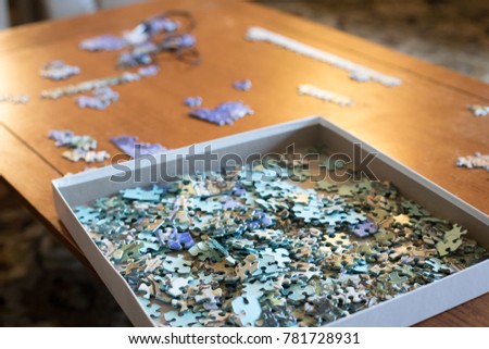 Low angle view of an unsolved puzzle, with pieces piled in a square box made of cardboard, on a wood coffee table
