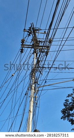 Low angle view of an urban utility pole with overhead power lines, electrical cables, ceramic insulators, and distribution equipment against a clear blue sky.