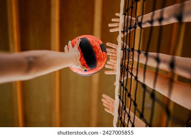 Low angle view of a volleyball players' hands blocking a ball over the net on training. Close up of sportswomen hands with a volleyball blocking it over the volleyball net during the training. - Powered by Shutterstock