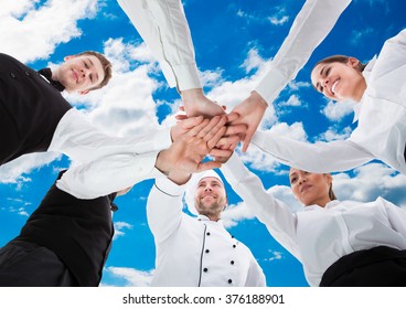 Low angle view of waiters and waitresses stacking hands against sky