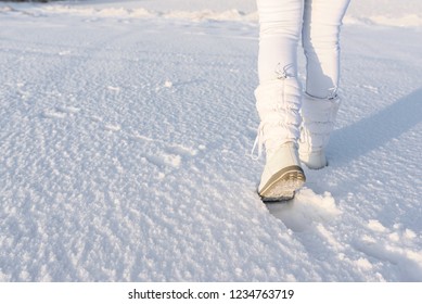 Low Angle View Of Walking Away Female Legs With White Snow Boots On, In Deep Snow. Winter Background.