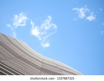 Low angle view of a wavy facade detail of a small modern office building, white construction against a large patch of light blue sky and delicate white cloud.