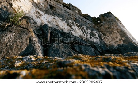 Low angle view of a weathered stone fortress wall, with a focus on the textured, moss-covered ground in the foreground.