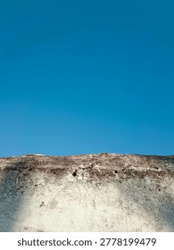 low angle view of a weathered white concrete wall contrasting against a clear vibrant blue sky under bright natural sunlight
