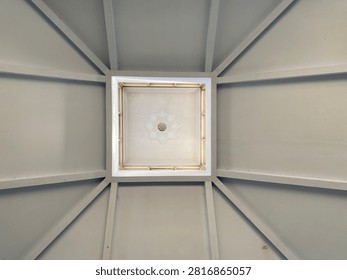 Low angle view of white building ceiling with geometric structural beams and central skylight