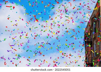 Low angle view of a white clouded blue sky filled with colorful confetti or streamers during a street parade with building out of focus in the background - Powered by Shutterstock