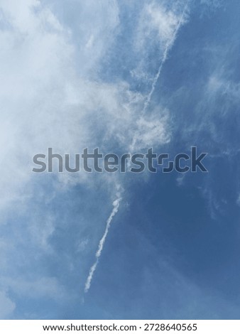 Low angle view of a white contrail cutting through a blue sky with soft clouds.