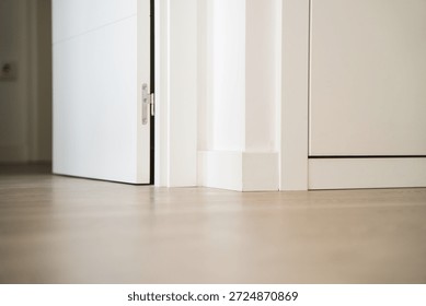 Low angle view of white interior door opening onto light wooden floor, minimalist apartment detail with baseboards and clean modern design