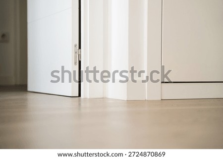 Low angle view of white interior door opening onto light wooden floor, minimalist apartment detail with baseboards and clean modern design