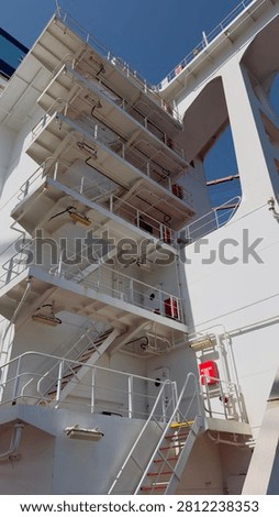 Low angle view of a white multi level superstructure with stairs on a cargo ship deck against blue sky