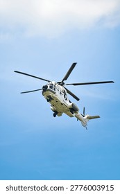 Low angle view of a white twin-engine transport helicopter flying against a clear blue sky.