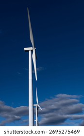 Low Angle View of White Wind Turbines Against Deep Blue Sky and Grey Clouds