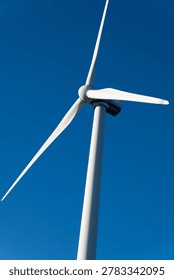 A low angle view of a white wind turbine against a clear, deep blue sky, representing sustainable energy and modern technology.