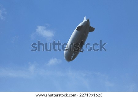 A low angle view of a white zeppelin in the blue clear sky