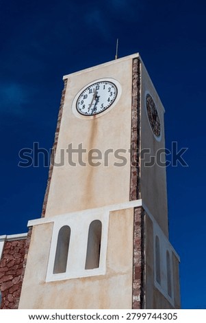 Low angle view of a whitewashed Greek clock tower with arched windows under clear blue sky, Santorini island architecture and travel concept.