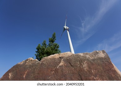 A Low Angle View Of A Wind Turbine The Cliff Near The Tree On A Sunny Day