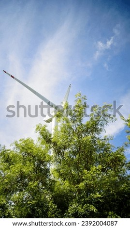 Low angle view of the wind turbine on Lamma island in Hong Kong with the green tree in the foreground. A tree cover the wind turbine. Rural scene.