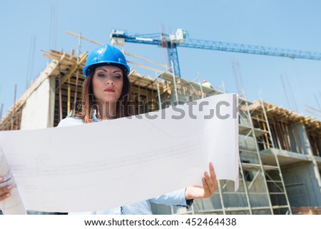 Low angle view of woman engineer with architectural plan in the hands.Construction site in the background