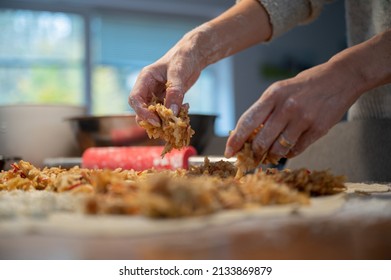 Low angle view of a woman making traditional homemade apple strudel dropping the filling on a rolled pastry dough.
