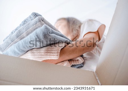 Low angle view of a woman sorting clothes and putting stack of knitted sweaters in a box for selling, donation or recycling. Sustainably kind living. Conscious and environmentally consumption. 