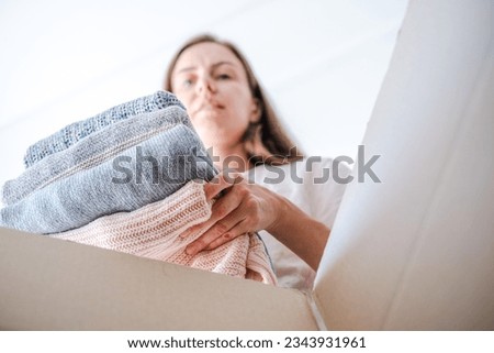 Low angle view of a woman sorting clothes and putting stack of knitted sweaters in a box for selling, donation or recycling. Sustainably kind living. Conscious and environmentally consumption. 