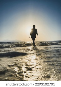 Low angle view of woman walking in backlit on a beach at sunset against blue sky - Shutterstock ID 2293102701
