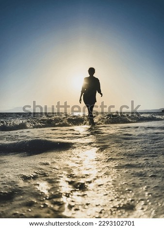 Low angle view of woman walking in backlit on a beach at sunset against blue sky