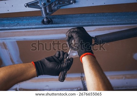 Low angle view of a worker fastening a spring on a garage door mechanism during installation or repair.	