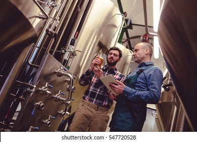 Low angle view of worker and owner discussing over beer in container at brewery - Powered by Shutterstock