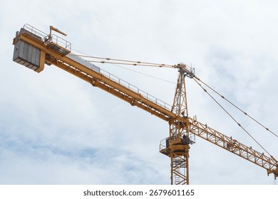 Low angle view of yellow construction tower crane boom extending horizontally against overcast sky. Heavy lifting equipment and machinery used for high-rise building
