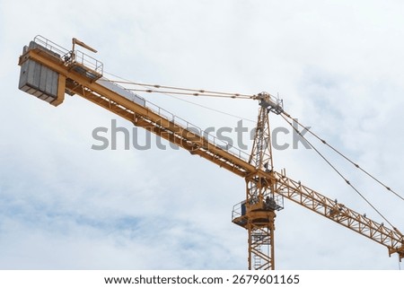 Low angle view of yellow construction tower crane boom extending horizontally against overcast sky. Heavy lifting equipment and machinery used for high-rise building