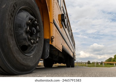 Low angle view of yellow school bus - detailed tire and body - cloudy sky backdrop. Taken in Toronto, Canada.
