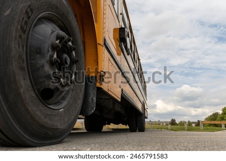 Low angle view of yellow school bus - detailed tire and body - cloudy sky backdrop. Taken in Toronto, Canada.