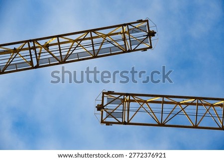 Low angle view of yellow tower crane jibs against a clear blue sky. High-quality industrial imagery representing construction, engineering, and urban development.