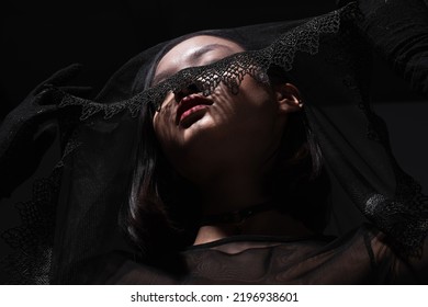 Low Angle View Of Young Asian Woman In Black Gloves Holding Black Veil Isolated On Grey