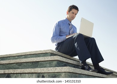 Low angle view of young businessman using laptop while sitting on marble staircase against clear sky - Powered by Shutterstock