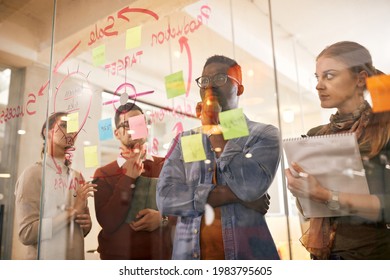 Low angle view of young creative business team thinking of new ideas while making mind map on glass wall in the office. Focus is on black businessman. The view is through the glass.