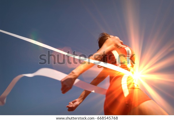 Low angle view of young female athlete\
crossing finish line against clear blue\
sky