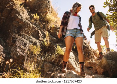Low angle view of young man and woman walking over a rocky mountain trail. Couple hiking through extreme terrain.