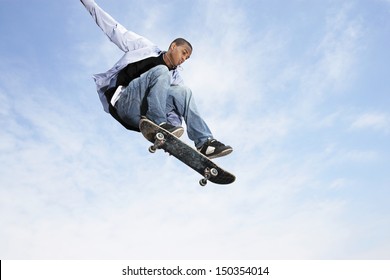 Low angle view of young man on skateboard in midair against cloudy sky