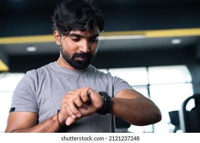 Low Angle View Of Young Man Monitoring Calories Or Heart Rate From Smartwatch At Gym - Concpet Of Wearable Technology, Healthcare And Active Fitness Lifestyle.