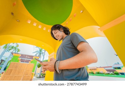 Low angle view of young man using cell phone outdoors. Smiling latin guy texting with cell phone in Nagarote park