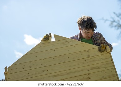 Low Angle View Of A Young Man Assembling A Wooden Playhouse In A DIY Concept.