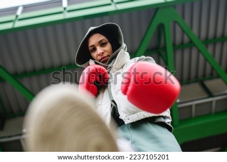 Low angle view of young muslim woman with boxing gloves standing outdoor in city.
