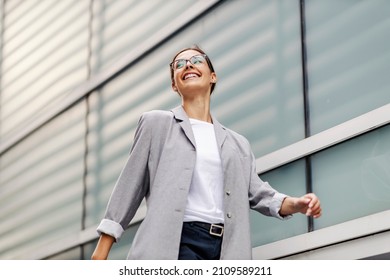 Low angle view of young, smiling businesswoman dressed elegantly passing by windows and going to her office. A successful businesswoman going to her workplace