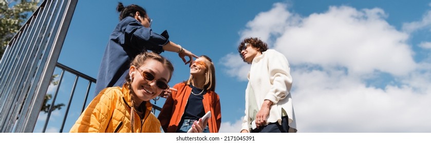 low angle view of young woman smiling at camera near interracial friends against cloudy sky, banner - Powered by Shutterstock