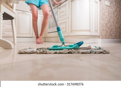 Low Angle View Of Young Woman Mopping Kitchen Floor With Focus On Shiny Clean Floor And Mop