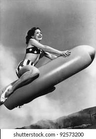 Low angle view of a young woman sitting on a rocket and smiling