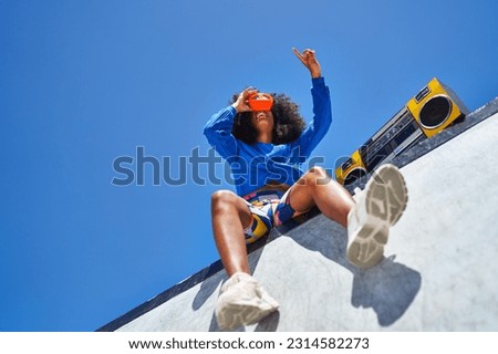 Low angle view young woman with boom box using view finder toy, looking up at sunny blue sky