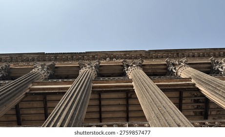 A low angle, wide perspective showcasing numerous grand weathered stone columns with ornate capitals and an elaborate cornice of a historic building.
